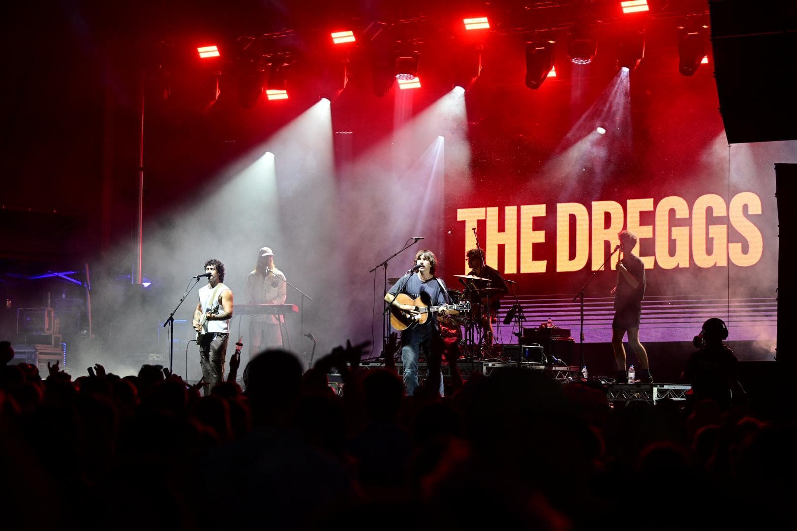 Band performing on stage with red lights and "The Dreggs" displayed in the background. Crowd silhouettes in the foreground.