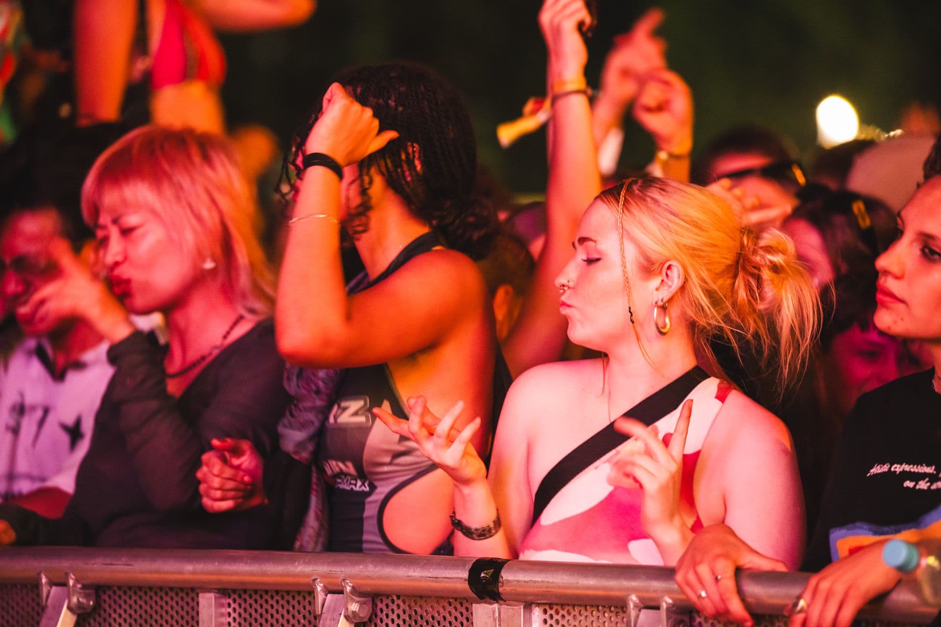 A lively crowd at a concert, with people dancing and enjoying the music near the stage barrier.