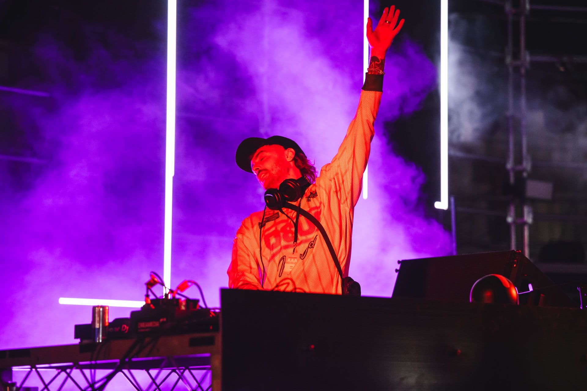 DJ performing energetically on stage with vibrant purple lighting and vertical light beams in the background.