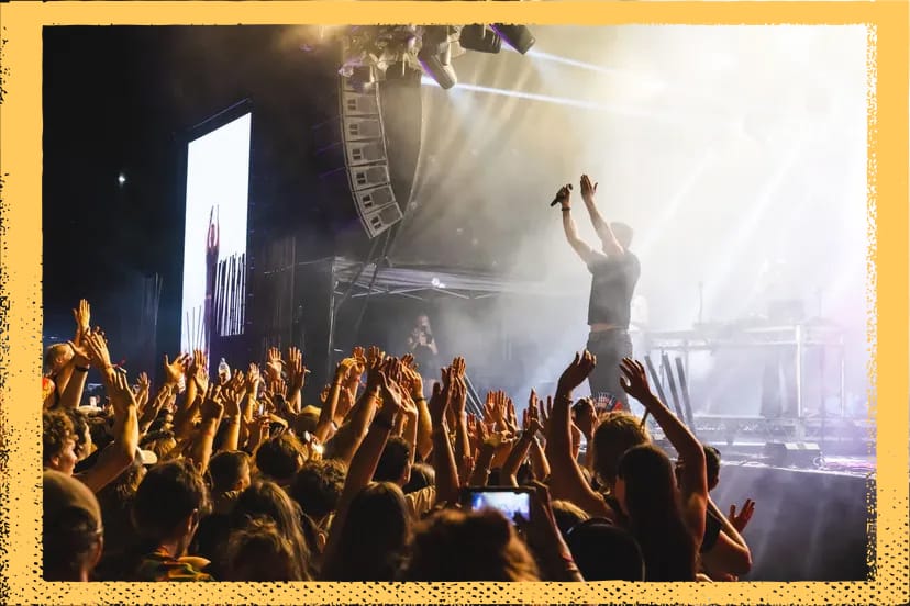 Concert scene with a singer on stage holding a microphone, surrounded by bright lights and a crowd with raised hands, capturing the lively atmosphere.